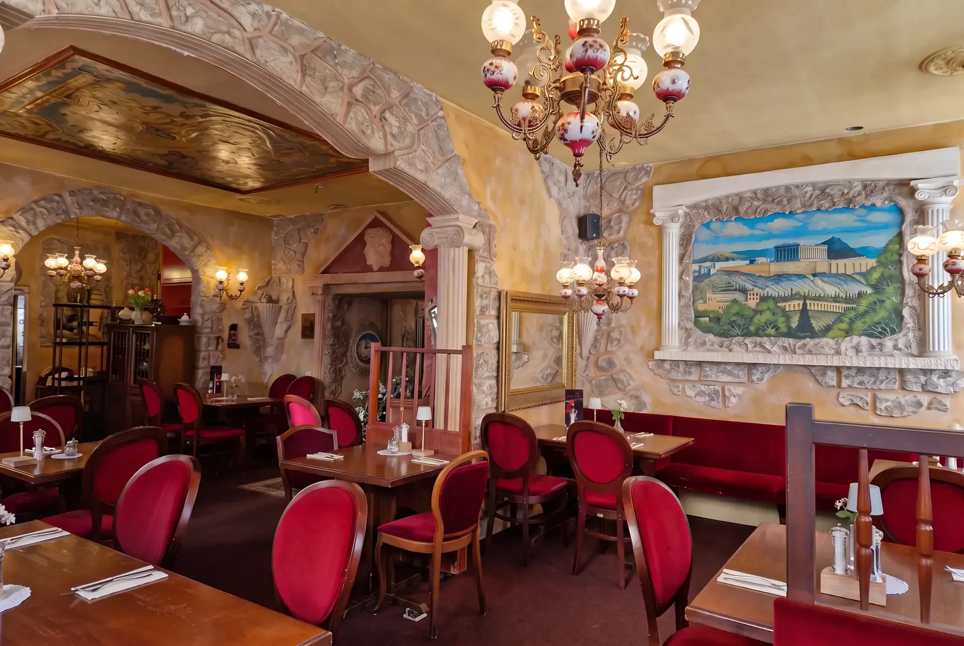 Innenraum des Restaurant Olympia mit roten Stühlen, Steinbögen und Akropolis-Gemälde